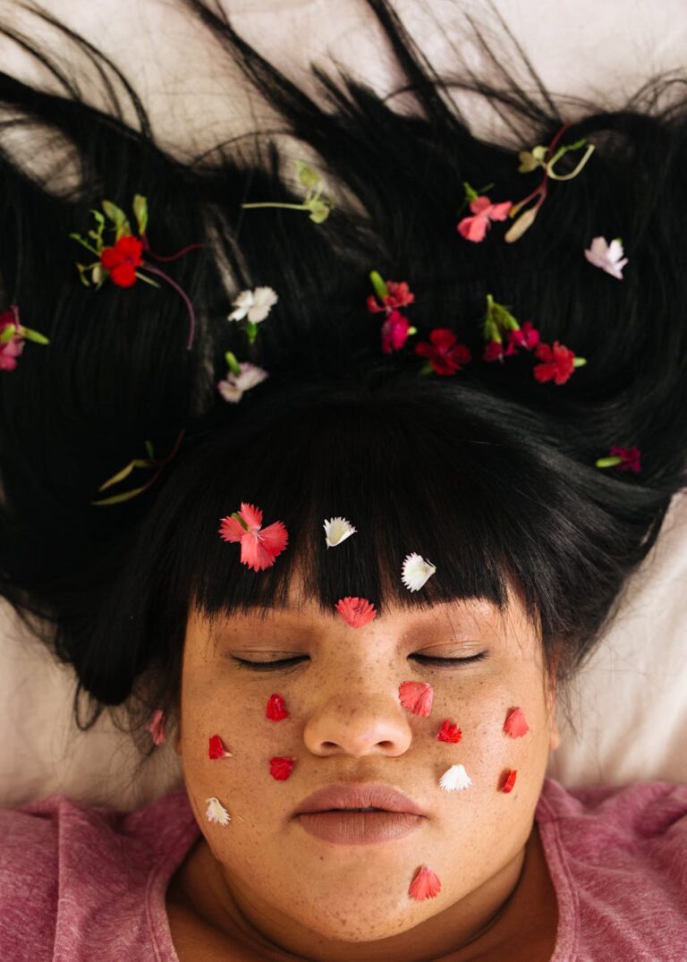 sensual young overweight ethnic lady with flower petals and closed eyes lying on bed